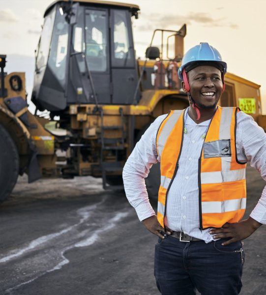 A young Black African coal mine foreman looking off camera laughing wearing reflective bib and hard hat after a long day of work on site at the coal mine