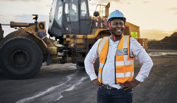 A young Black African coal mine foreman looking off camera laughing wearing reflective bib and hard hat after a long day of work on site at the coal mine