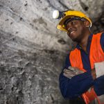 African American miner working at the mine and wearing a helmet with the light on in a dark tunnel